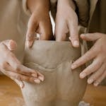 Close-up of hands molding a clay pot, showcasing artisan skills and craftsmanship.